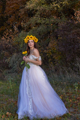 Fototapeta na wymiar Beautiful cute sexy girl in a white dress with a wreath of sunflowers on her head enjoying nature. Autumn time.