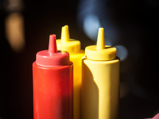 Three plastic bottles, red and yellow, used for fast food sauces such as ketchup and mustard, on display on a restaurant table with a black background