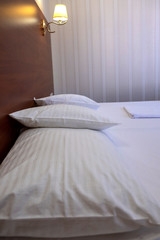 A double bed with three pillows in the hotel room, covered with white linen.
