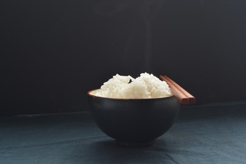 A small bowl of rice with chopsticks in front of a black background