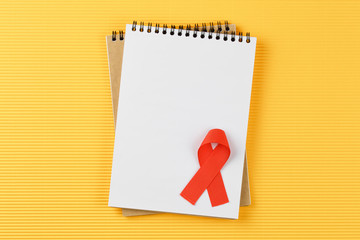 red aids ribbon on open notebook isolated on yellow background