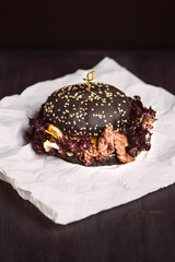 black bread burger with healthy meat and leaves of brown salad on paper