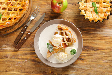 Plate with slice of tasty apple pie and ice cream on wooden table
