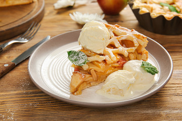 Plate with slice of tasty apple pie and ice cream on wooden table