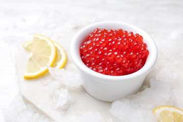 Red caviar in bowl with ice and lemon on light table