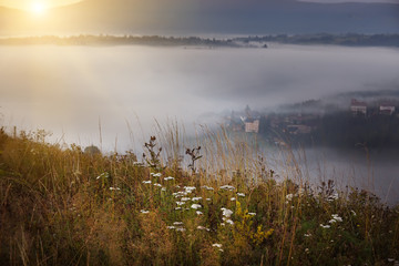 Beautiful sunrise in the mountains. A small village among the mountains in the fog, the red sky just before sunset and the silhouettes of the mountains. 
