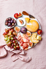 Appetizers, antipasti snacks. Cheese and fruit platter on marble board over pink linen tablecloth background. Top view