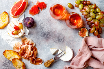 Appetizers, antipasti snacks and rose wine in glasses. Cheese and meat platter over grey concrete background. Frame, copy space, top view