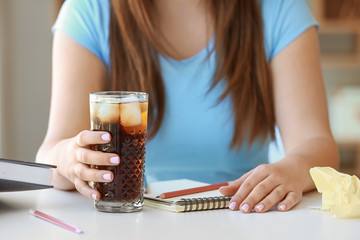 Woman with glass of cold cola sitting at table in office