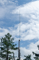 Obraz premium Lightning rod and coniferous tree top against blue sky with white clouds