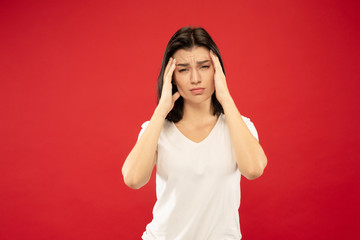 Caucasian young woman's half-length portrait on red studio background. Beautiful female model in white shirt. Concept of human emotions, facial expression. Suffering from headache, feeling ill.