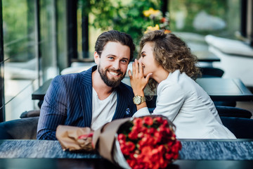 Happy loving couple is spending time together in modern restaurant. Attractive young woman and handsome man in suit are having romantic dinner. Celebrating Saint Valentine's Day. Secret time.