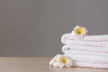 Stack of clean towels with flowers on table against grey background