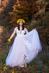 Beautiful cute sexy girl in a white dress with a wreath of sunflowers on her head enjoying nature. Autumn time.