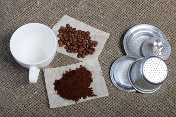 Ground coffee and coffee grains on a background of coarse linen cloth. Nearby details of a Vietnamese coffee maker and a cup. World Coffee Day.