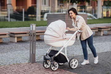 Side view of a Caucasian Mum walking on city street while pushing her toddler sitting in a pram. Family concept.