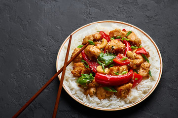 Schezwan Chicken or Dragon Chicken with basmati rice at black slate background. Szechuan Chicken is popular indo-chinese spicy dish with chilli peppers, chicken and vegetables.