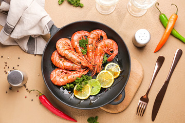 Frying pan with tasty shrimps on color background