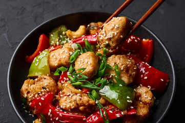 Schezwan Chicken or Dragon Chicken in black bowl at dark slate background. Szechuan Chicken is popular indo-chinese spicy dish with chilli peppers, chicken and vegetables.