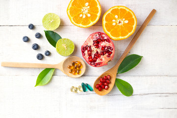 Multivitamin supplements on wooden spoon with healthy fruit blueberry, lime, orange, pomegranete on white wooden background.