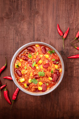 Chili con carne and chilli peppers, shot from the top on a dark rustic wooden background with a place for text