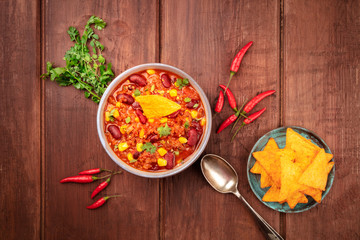 Chili con carne, shot from the top on a dark rustic wooden background with ingredients and nachos