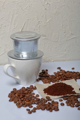 A cup of coffee with a Vietnamese coffee maker. Grains of coffee and a little ground coffee are scattered nearby on the table surface. World Coffee Day.