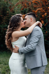 Fototapeta premium Young couple in love outdoor. Young couple in celebrate outfits among the branches of sea buckthorn. A loving couple, a guy and a girl kiss and hug. Happy lovers and family. Love story. 