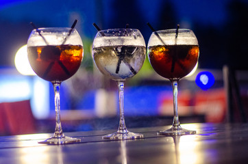 Beautiful row line of different colored alcohol cocktails on a party, martini, vodka,and others on decorated catering bouquet table on open air event, picture with beautiful bokeh