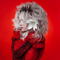 Shades of red. Attractive woman, in a red dress, posing on a red background, with white lily...