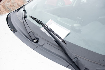 Close-up of a parking ticket on the outside of the car's windshield, under the wipers.