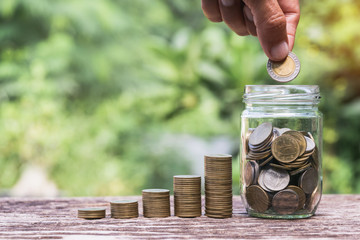 Coins in glass jar  Set on wooden plate, put in a green park background also some coins beside.