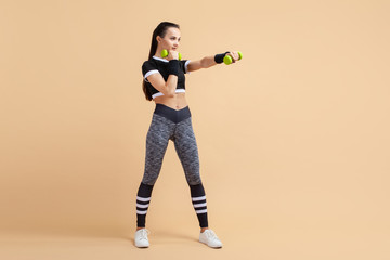 A young girl, a brunette with a ponytail, works out punches using extra weights, a full-length photo.