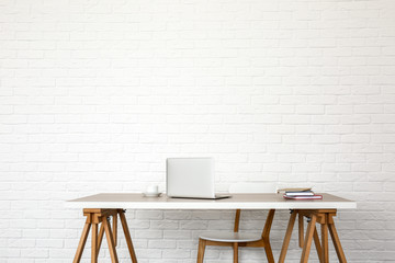 Table with modern laptop and chair near white brick wall