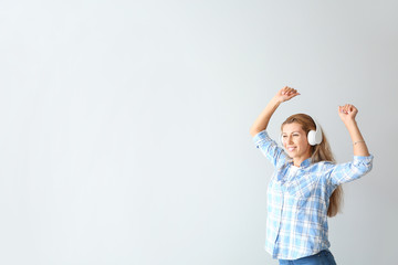 Dancing young woman with headphones on light background