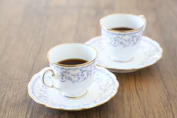 白い壁の背景に木製テーブル。その上に置かれたコーヒーカップ