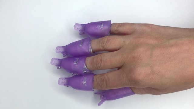 Plastic reusable cap clip for soak-off UV gel polish removal. Womens nails wrapped in cotton pads soaked in acetone and aluminium foil. Manicure process, removing gel nail polish on white background.