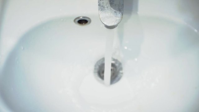 light faience sink with a metal mixer from which a stream of water flows.view from above.close-up.shallow depth of field.