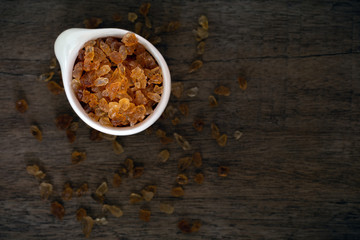 Natural organic brown crystal rock sugar in white ceramic cup over old wooden background.