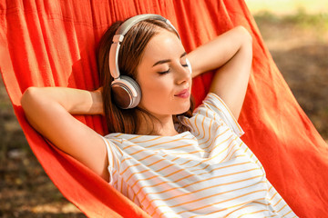 Beautiful young woman with headphones resting in hammock outdoors