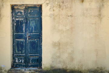 Old wooden door in cracked stone wall, copy space. The background is a battered cement wall with the texture of peeling paint