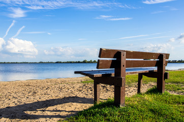 Empty brown bench by the beach overlooking a lake and blue sky with clouds in afternoon. Quiet place