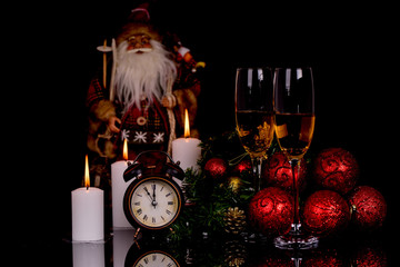 Two wine glasses with champagne, Santa Clause, clock and christmas ornaments on a black background with reflection