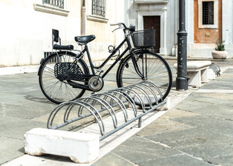 Fototapeta na wymiar Black bike mounted on a bicycle stand on italian street.