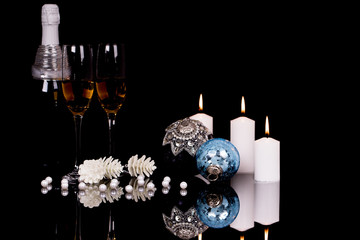 Two wine glasses with champagne, Christmas ornaments and candles on a black background
