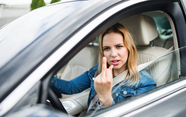 Fototapeta na wymiar Angry young woman driver sitting in car, showing middle finger.