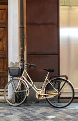 Fototapeta na wymiar Beige bike with basket on italian street. Typical italian architecture on background.