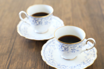 Fototapeta na wymiar 木製テーブルの上に乗った白い陶器のカップ&ソーサーにブラックコーヒー