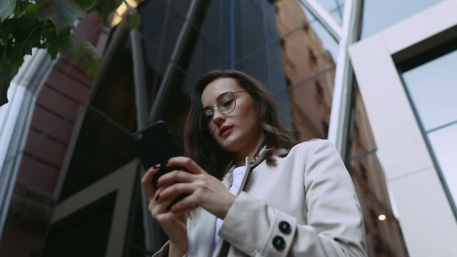 Adult Caucasian Confident Young Business Woman is Using Smartphone App Outside near Modern Office Building. Slow Motion Corporate Shot with Moving Camera Around