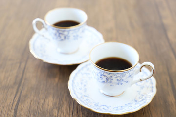 木製テーブルの上に乗った白い陶器のカップ&ソーサーにブラックコーヒー